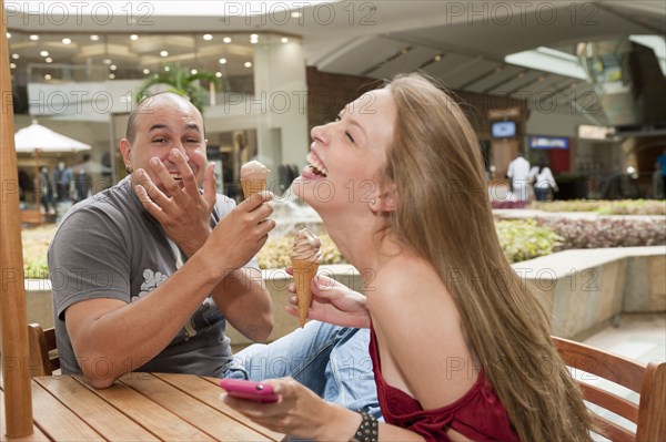 Laughing Hispanic couple eating ice cream cones in cafe