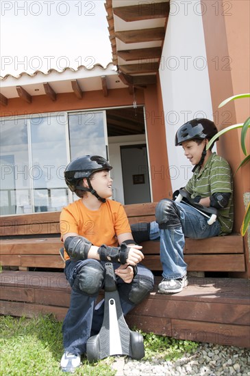 Hispanic boys in pads and helmets holding skateboards