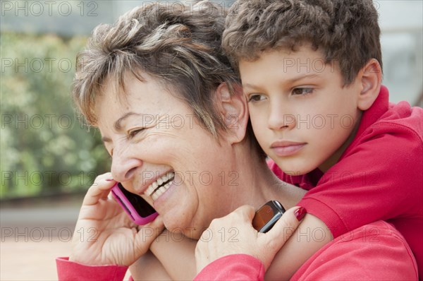 Hispanic boy hugging grandmother talking on cell phone