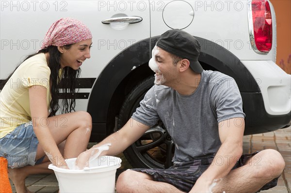 Playful Hispanic couple washing car together