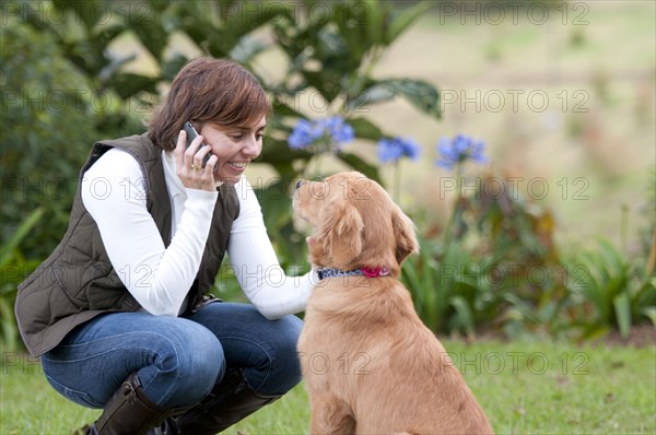 Smiling Hispanic woman talking on cell phone and petting dog