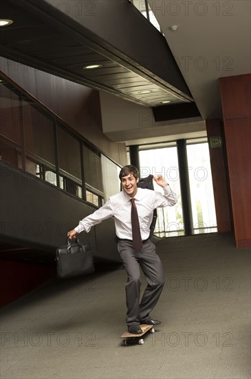 Hispanic businessman riding on skateboard