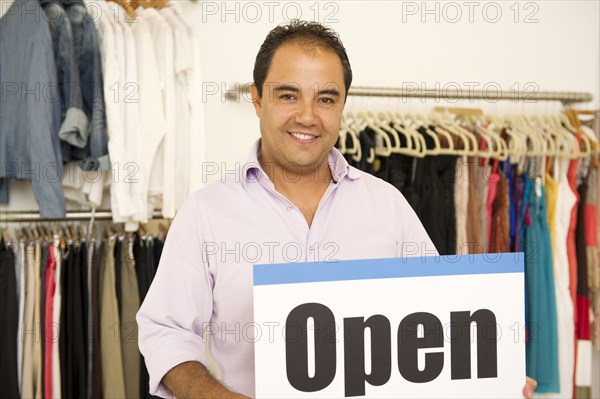 Hispanic man holding open sign in clothing store