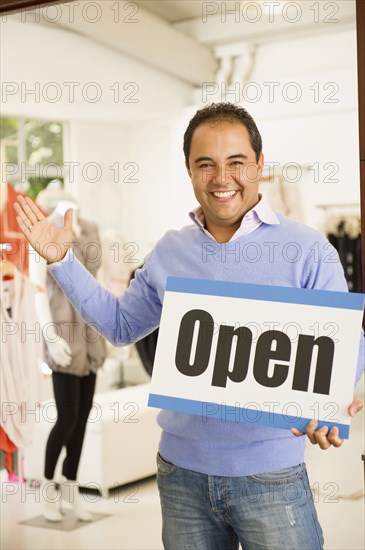 Hispanic man holding open sign in clothing store