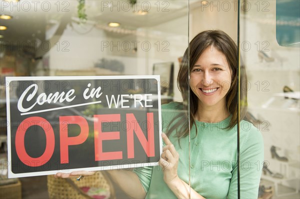 Hispanic woman holding open sign in shoe store