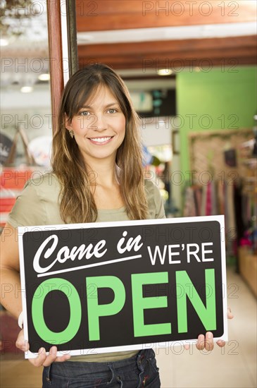 Hispanic woman holding open sign in store