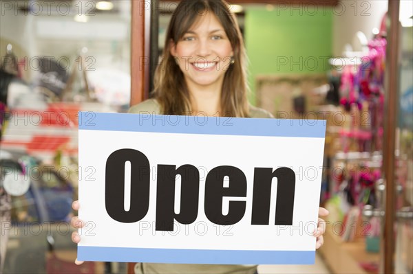 Hispanic woman holding open sign in store