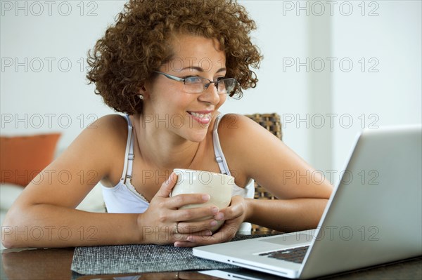 Hispanic woman drinking coffee and using laptop