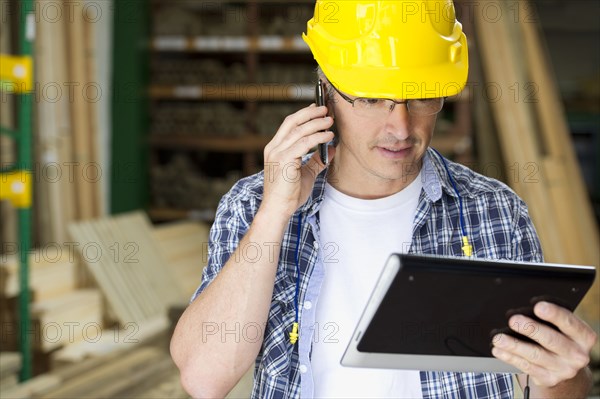 Hispanic carpenter using cell phone and digital tablet