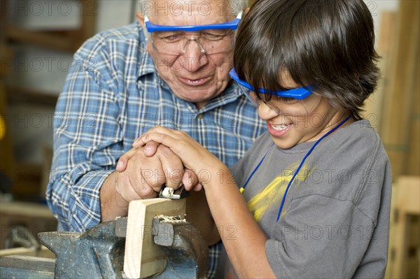 Hispanic grandfather and son planing wood in workshop