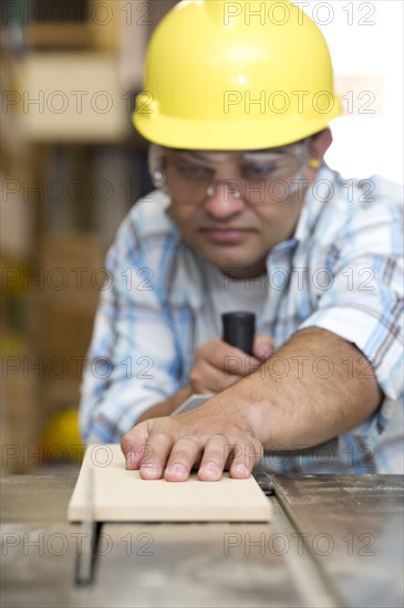 Hispanic carpenter cutting wood with table saw