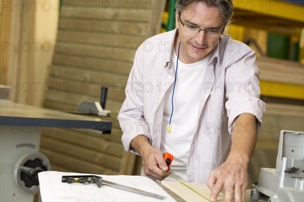 Hispanic carpenter measuring wood in workshop