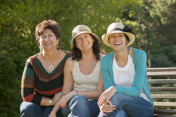 Hispanic mother and daughters sitting on bench