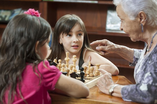 Hispanic grandmother and granddaughters playing chess