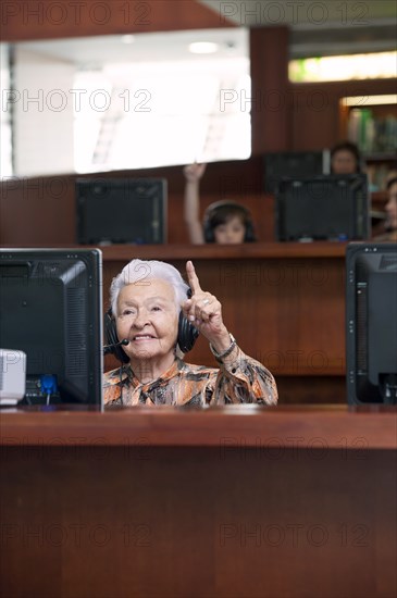 Senior Hispanic woman raising hand in computer lab