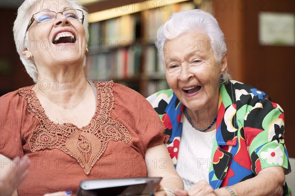 Senior Hispanic woman laughing and using digital tablet