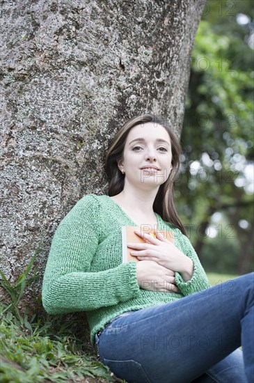 Hispanic woman reading by tree outdoors