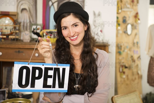 Hispanic woman holding 'open' sign in shop