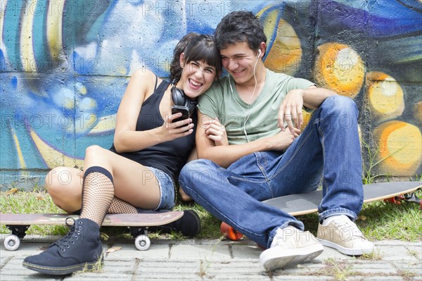 Hispanic couple sitting on skateboards