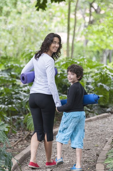 Hispanic mother and son walking with yoga mats in park