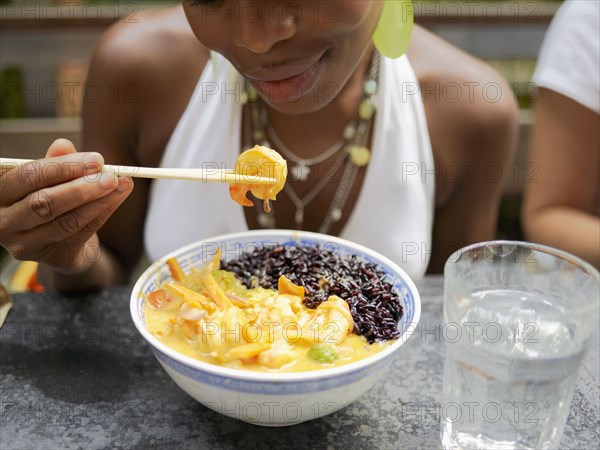 African woman eating Asian food in restaurant