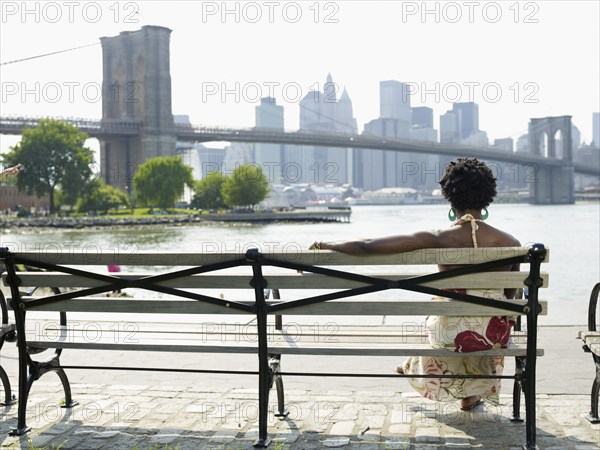 African woman sitting on bench at urban waterfront