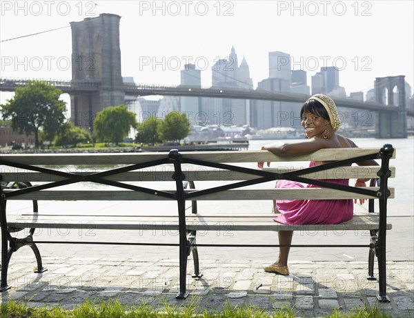 African woman sitting on bench at urban waterfront