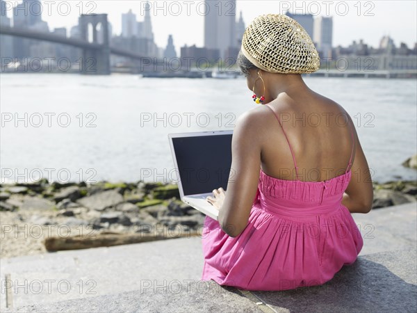 African woman sitting at urban waterfront typing on laptop