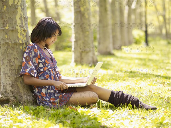 Hispanic woman typing on laptop in park