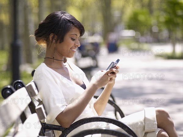 Hispanic woman text messaging on cell phone in park