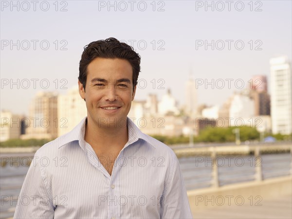 Man standing at waterfront with cityscape in background