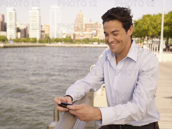 Man at waterfront text messaging on cell phone