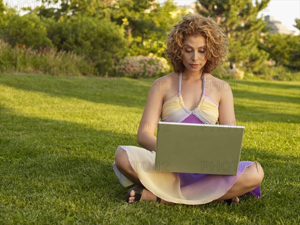 Mixed race woman typing on laptop in park