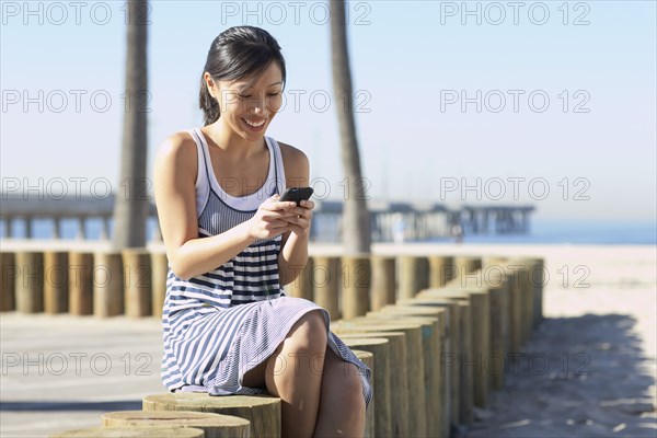 Asian woman sitting at beach using cell phone