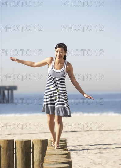 Asian woman balancing on posts at beach