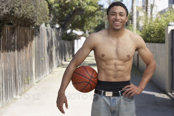 Young mixed race man with bare chest holding basketball