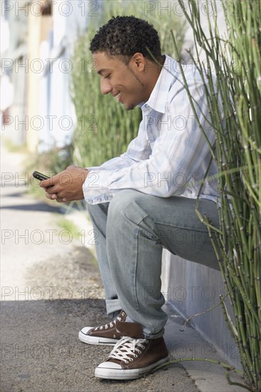 Young mixed race man sitting outdoors with cell phone