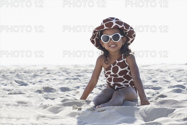 Young mixed race girl in sunglasses sitting at beach