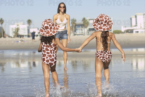 Young mixed race girls running to mother at beach