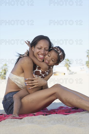 Mixed race mother hugging daughter at beach