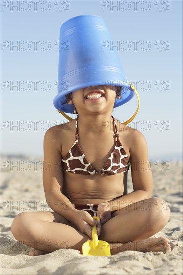 Young mixed race girl with bucket on head at beach