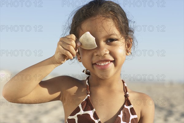 Young mixed race girl holding shell at beach