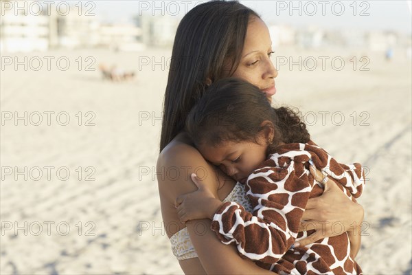 Mixed race mother holding daughter at beach