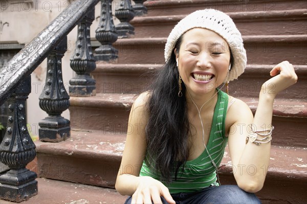 Asian woman sitting on front steps listening to music