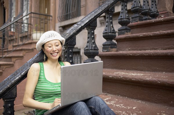 Asian woman sitting on front steps with laptop