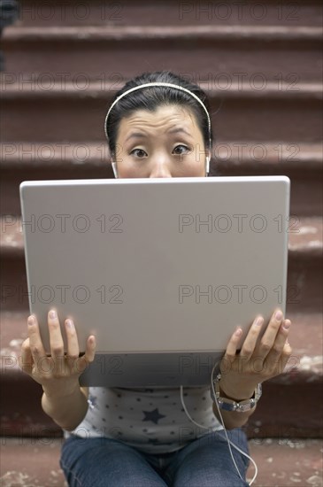 Asian woman sitting on front steps with laptop