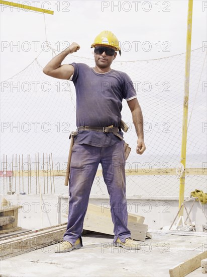 Hispanic worker flexing biceps on construction site