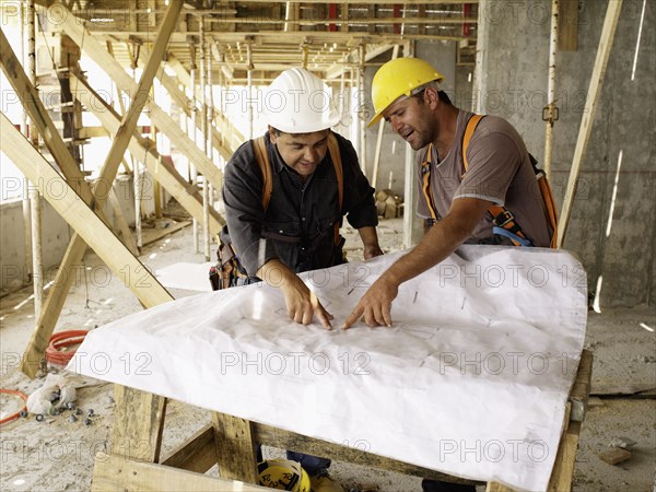 Hispanic workers looking at blueprints on construction site
