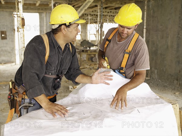 Hispanic workers looking at blueprints on construction site