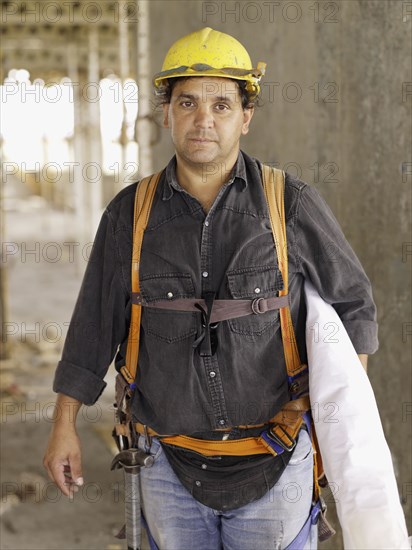 Hispanic worker holding blueprints on construction site